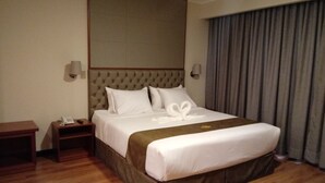 Una habitación de hotel con una cama grande, una mesita de noche de madera, un teléfono y una lámpara de pared.