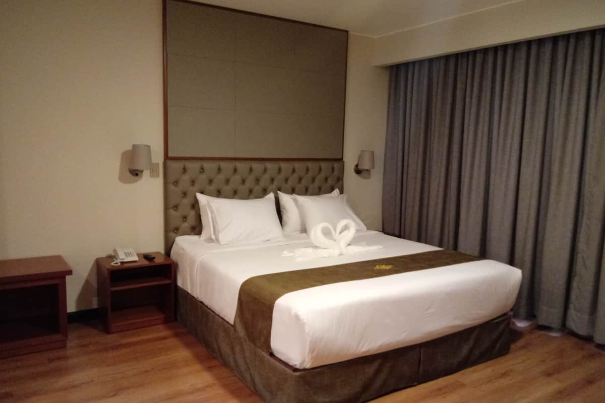 A hotel room with a large bed, a wooden nightstand, a telephone, and a wall-mounted lamp.