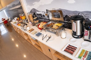 A buffet with various food items, a coffee machine, and a milk jug.