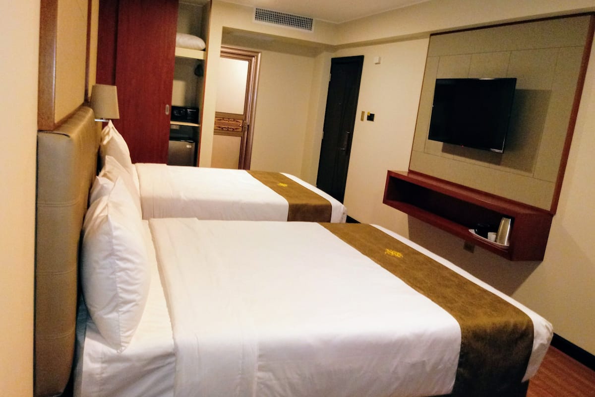 A hotel room with two beds, a TV, a minibar, and a door leading to a bathroom.