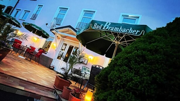 A hotel with a blue facade, outdoor seating area with umbrellas, and a sign for "Bad Brambacher". - Pension Nadia (Adorf)