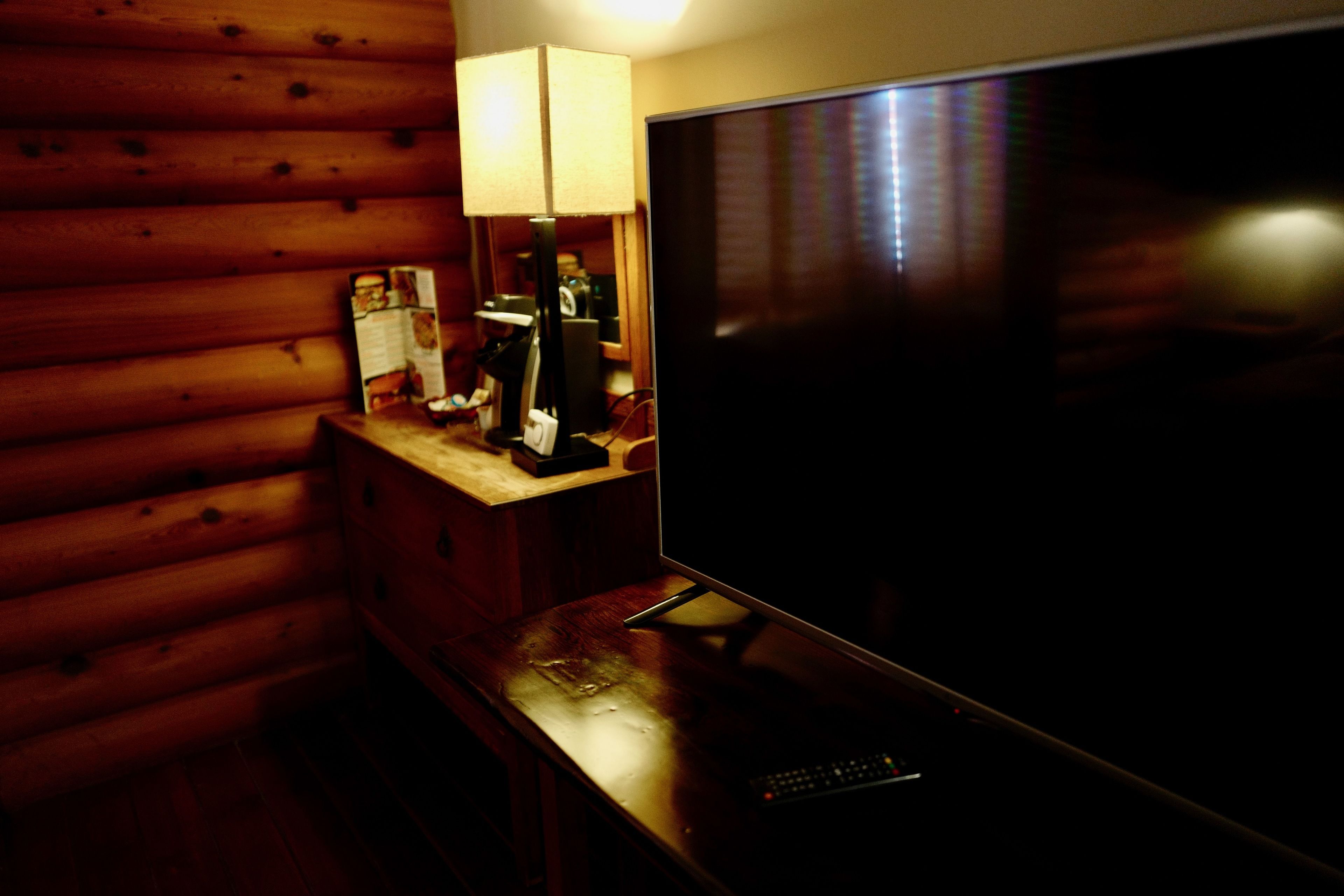 L’intérieur d’un chalet en bois, avec une télévision posée sur une table en bois, une lampe et une télécommande.