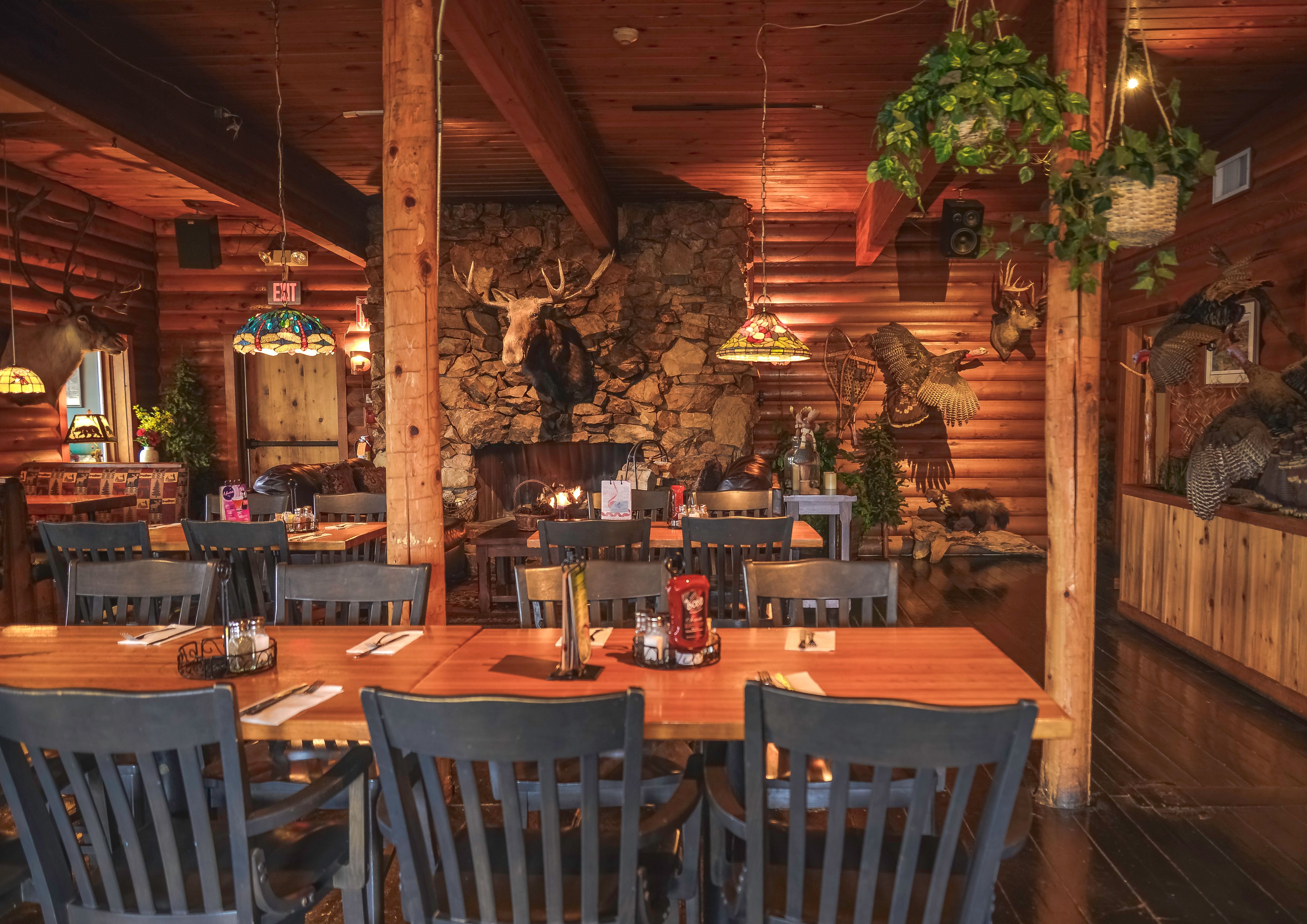 A rustic wooden interior with a stone fireplace, wooden tables and chairs, and various animal decorations.