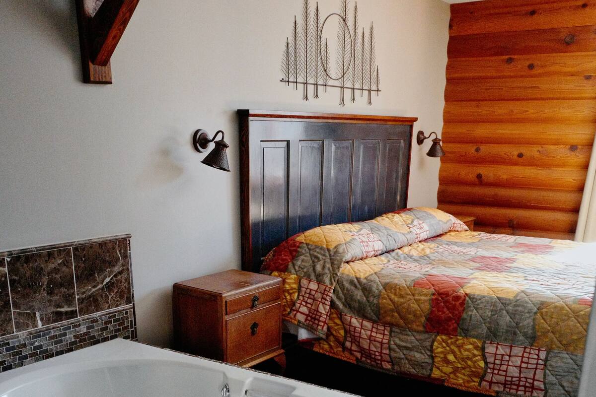 A bathroom with a large bathtub, a wooden headboard, a quilted bedspread, and a small wooden chest of drawers.