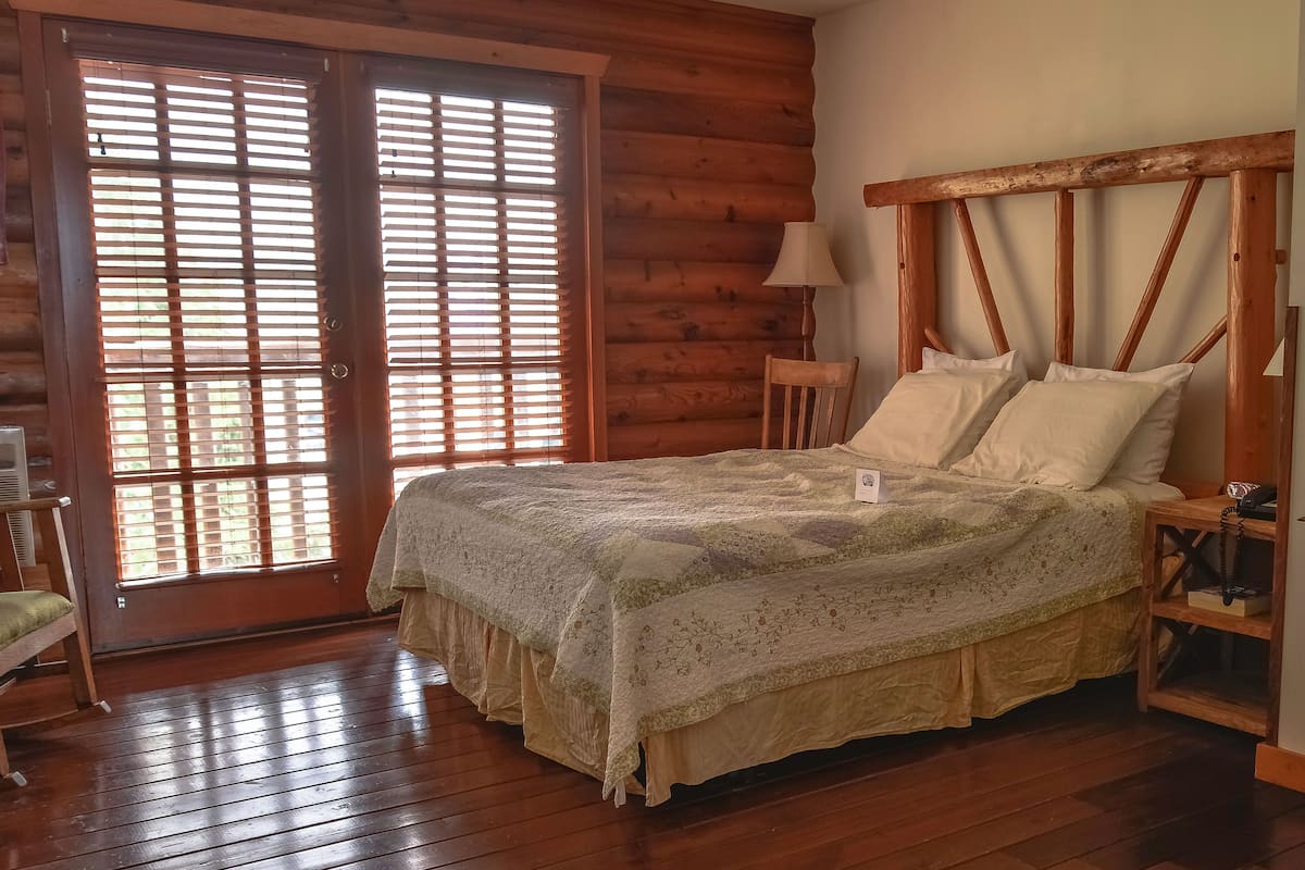 A wooden room with a bed, a chair, and a lamp.