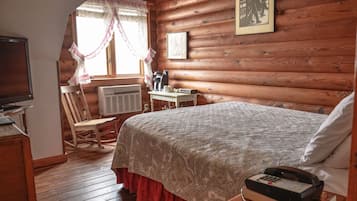 A cozy log cabin bedroom with a bed, a chair, a table with a coffee maker, and a television.