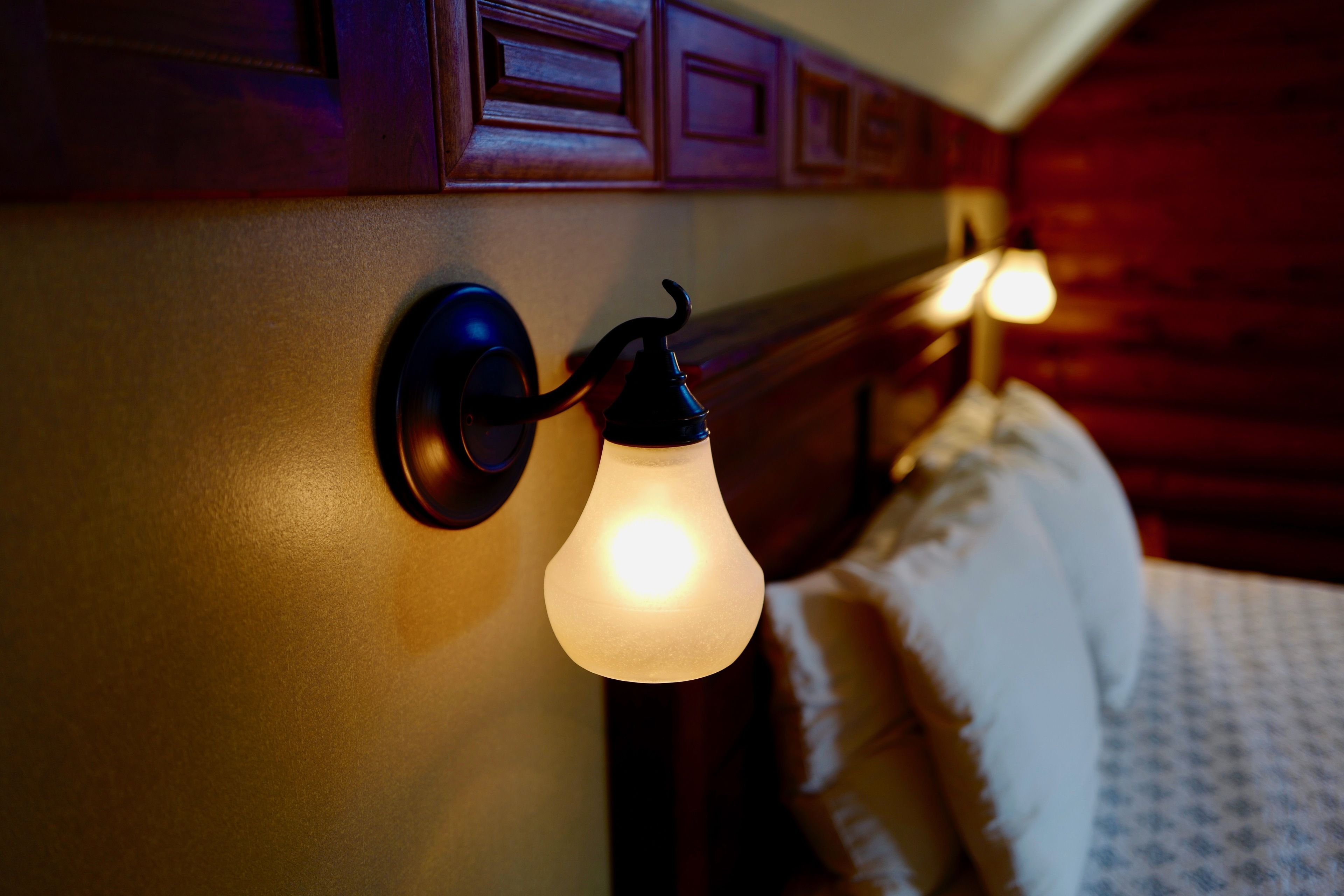 A wall-mounted light fixture with a bulb, a wooden headboard, and a bed with a patterned bedspread.