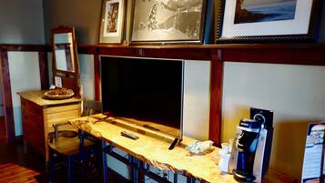 Una zona de bar con mostrador de madera, un televisor, una máquina de café y cuadros en la pared.