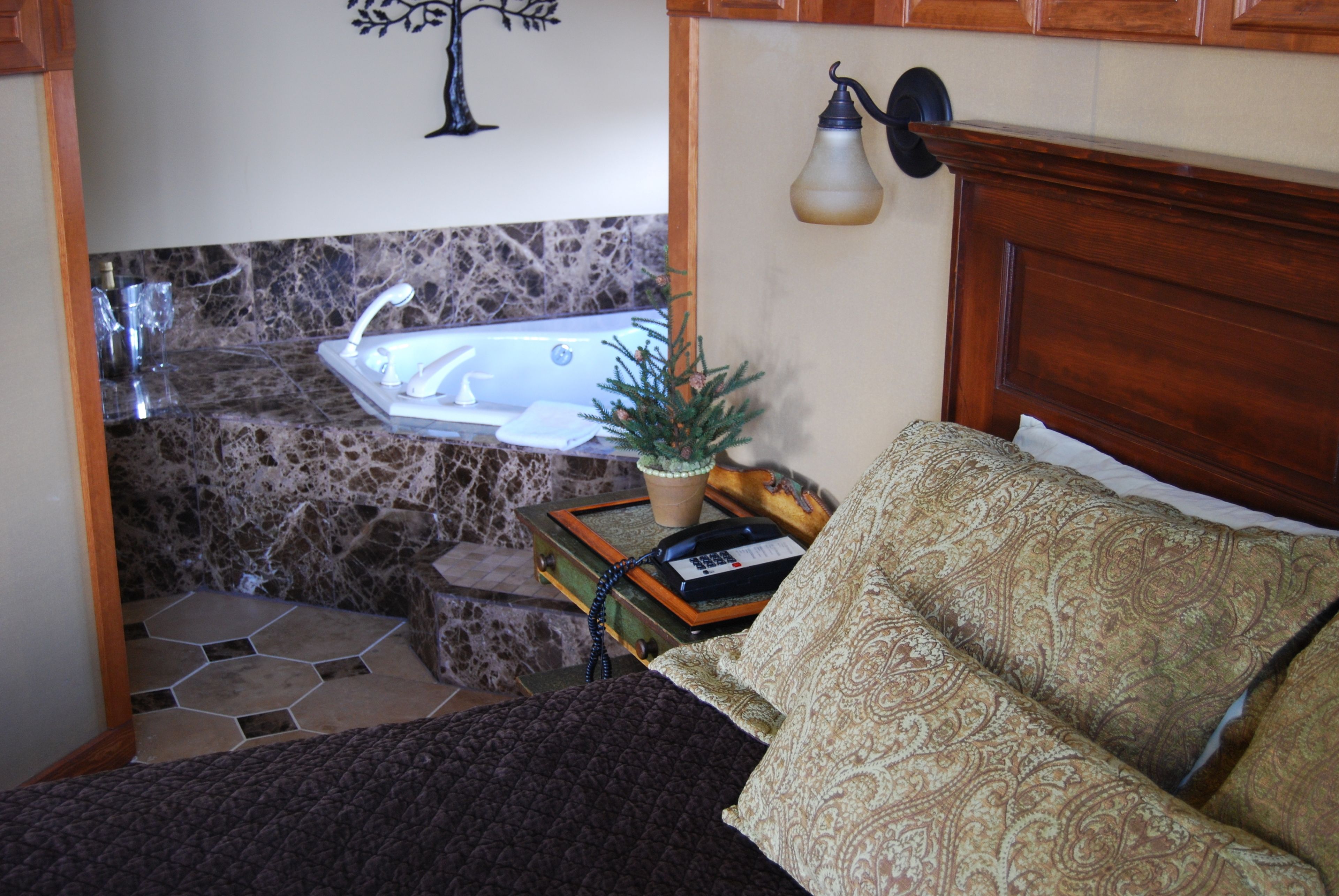 Une chambre à coucher de taille modeste, comprenant un lit, une table de chevet, une petite table avec une plante, une lampe et un téléphone d’époque.