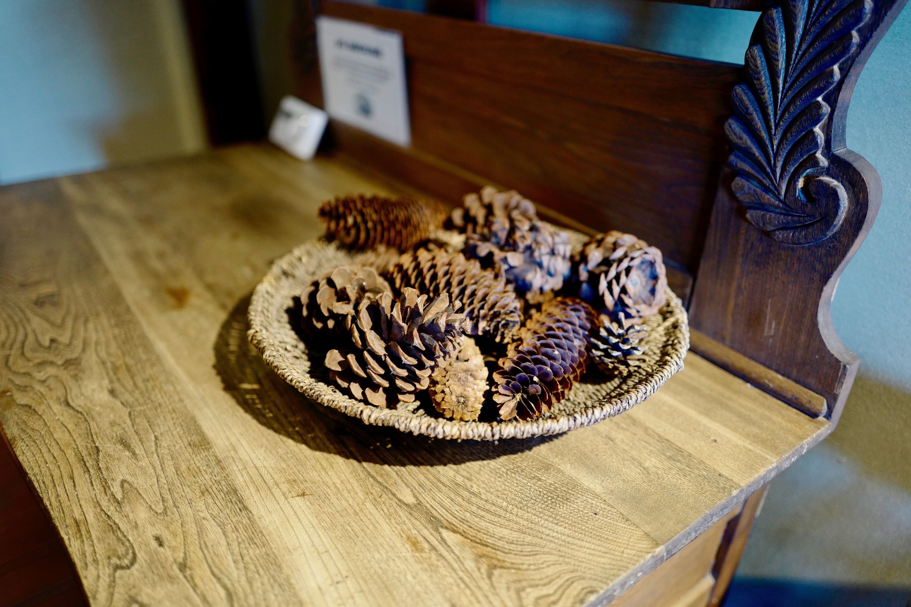 A wooden table with a woven basket containing pine cones.
