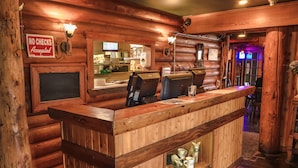 Un mostrador de recepción de madera con un cartel que dice 'NO SE RECIBEN CHEQUES', una caja registradora y una pequeña estantería con objetos decorativos.