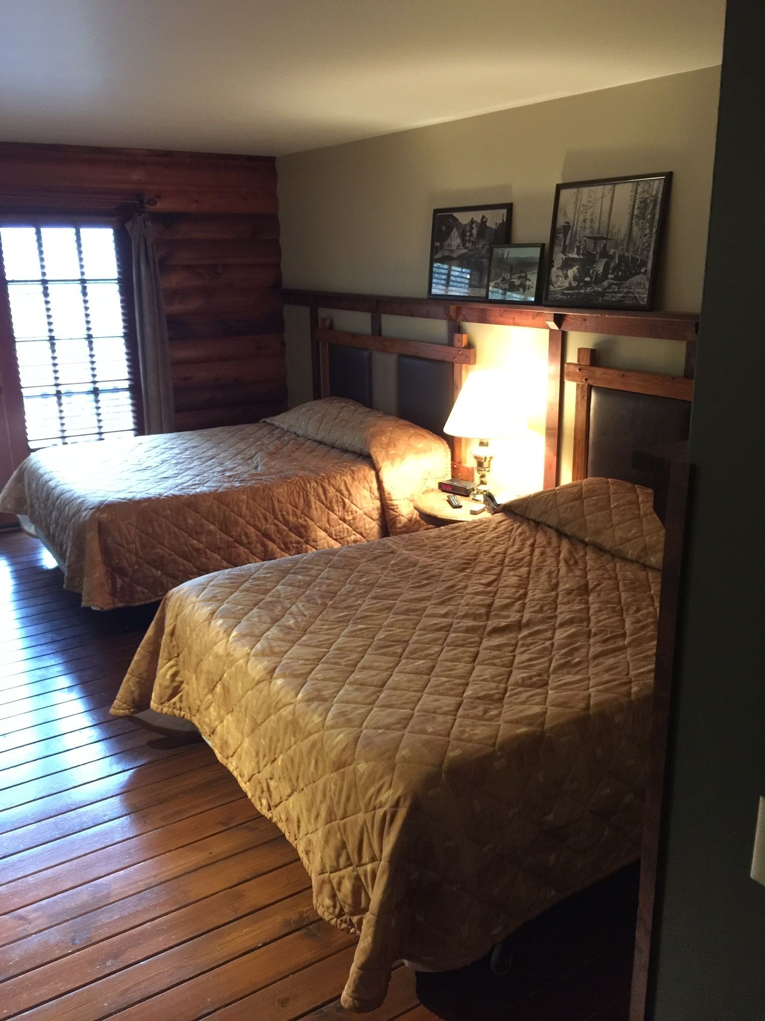 Deux lits simples avec des têtes de lit en bois, un plancher en bois et une fenêtre avec des stores.