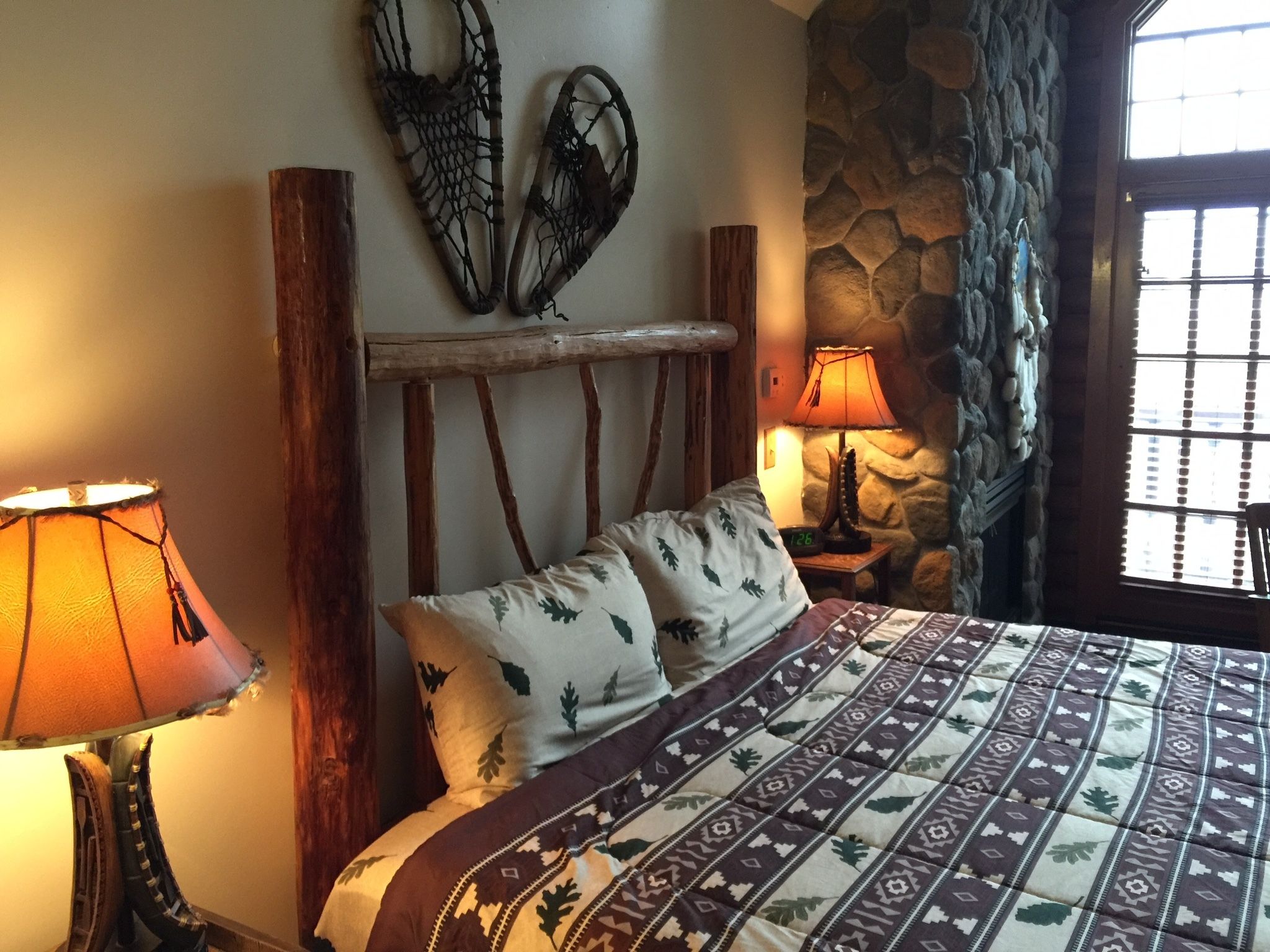 A bedroom with a wooden headboard, a patterned bedspread, a stone wall, and a window with a view.