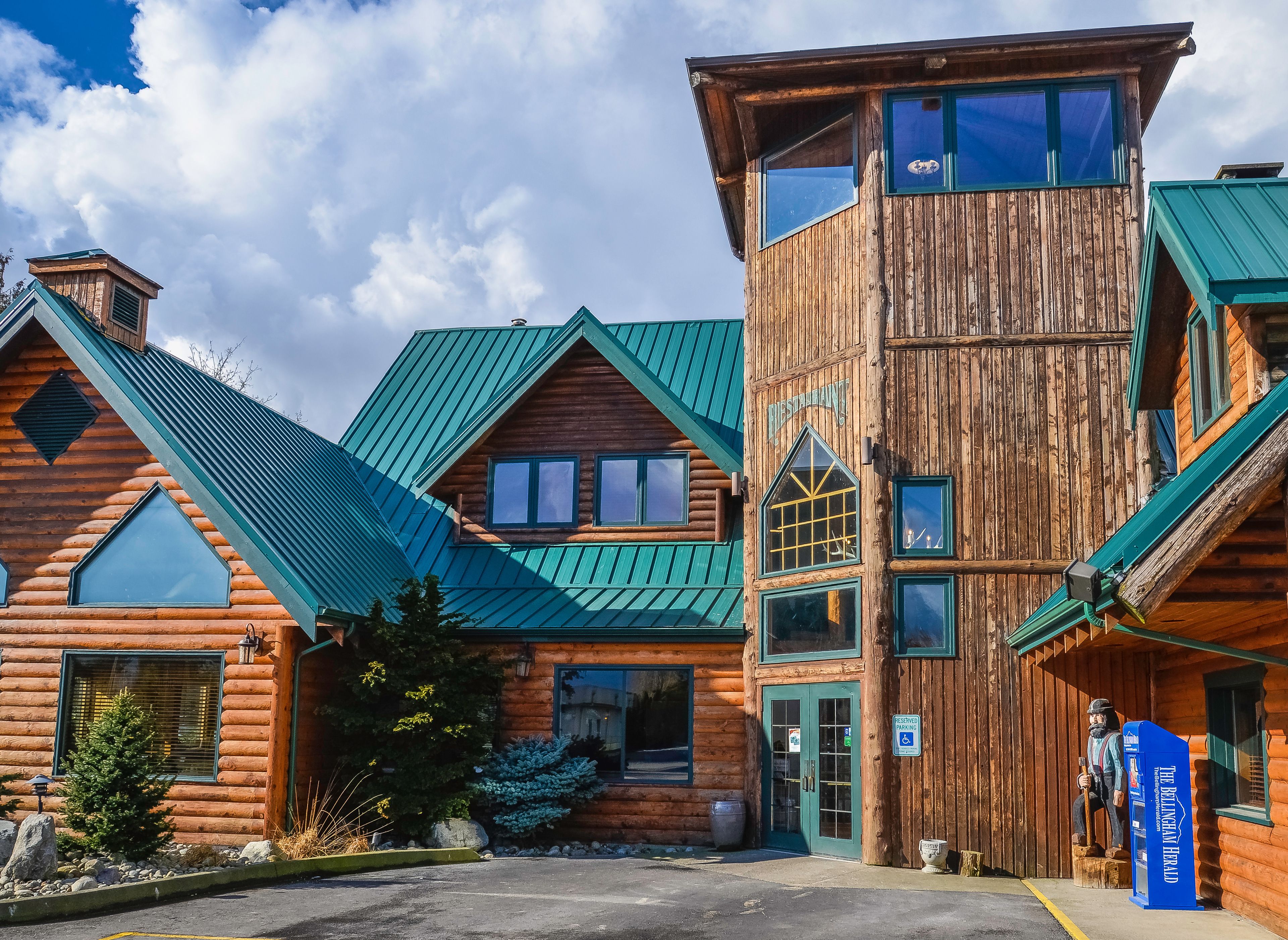 A log cabin-style building with a green metal roof, a visible entrance, and a sign indicating a restaurant.