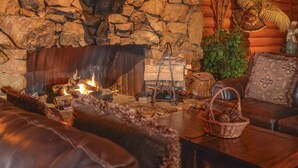 Un acogedor interior de cabaña con chimenea de piedra, sofás de cuero y una mesa de madera rústica.
