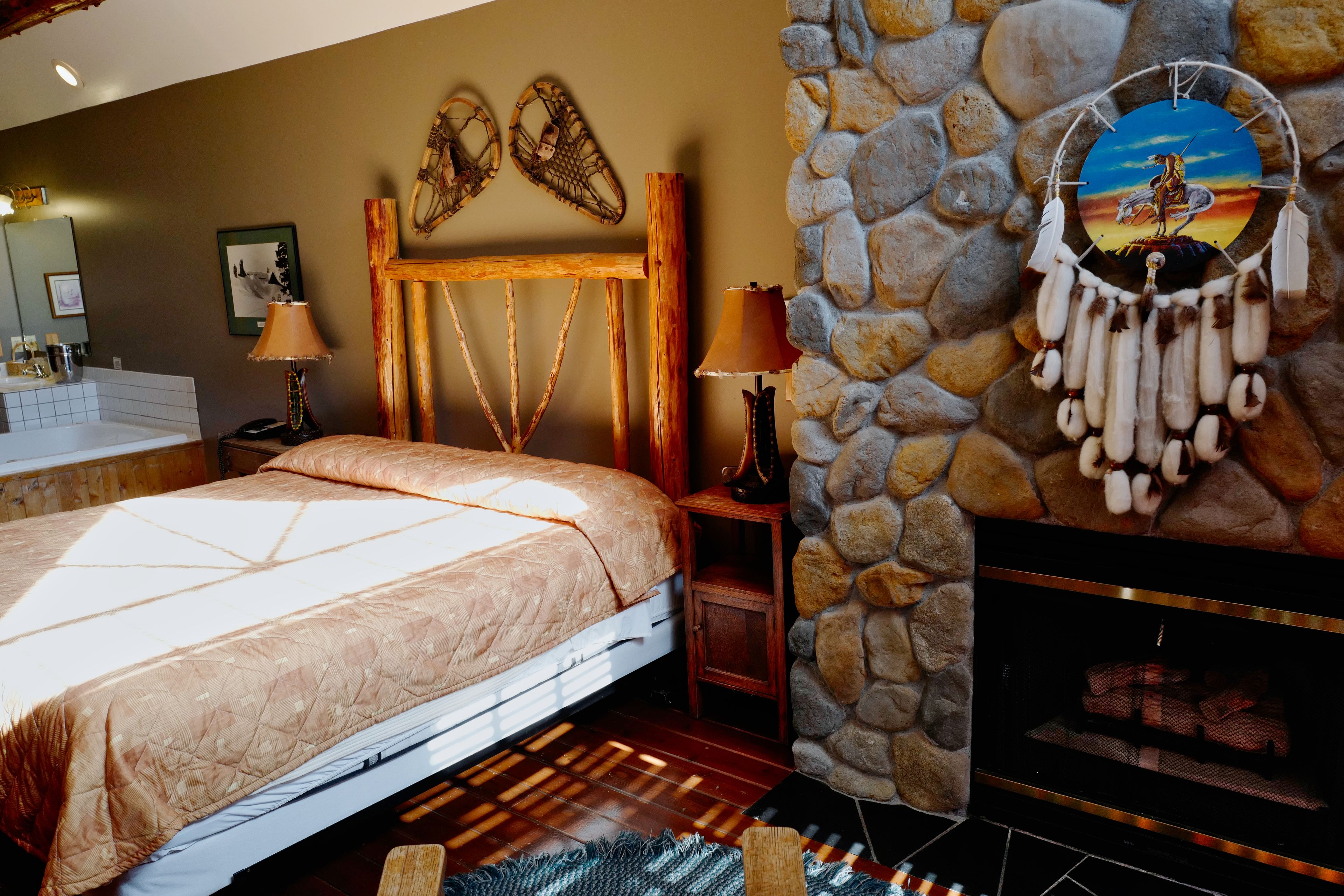 A bedroom with a bed, a stone wall, a fireplace, and a dreamcatcher.
