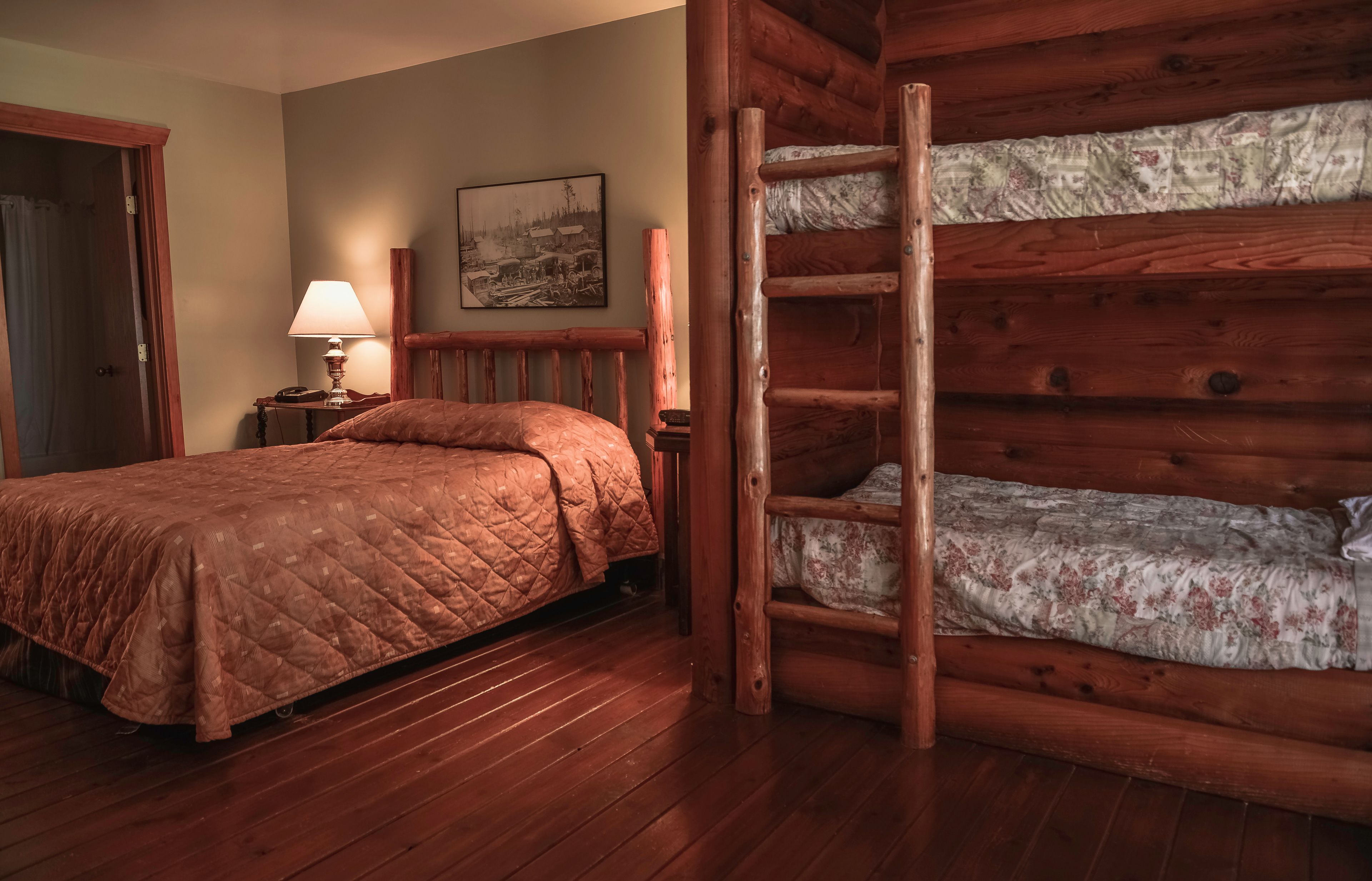 Ein holzgetäfeltes Zimmer im Blockhausstil mit einem Bett, einem Nachttisch, einer Lampe und einer Leiter zu einem Stockbett.