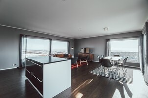 Um espaço de estar moderno com ilha de cozinha, área de refeições e amplas janelas com vista para a cidade.