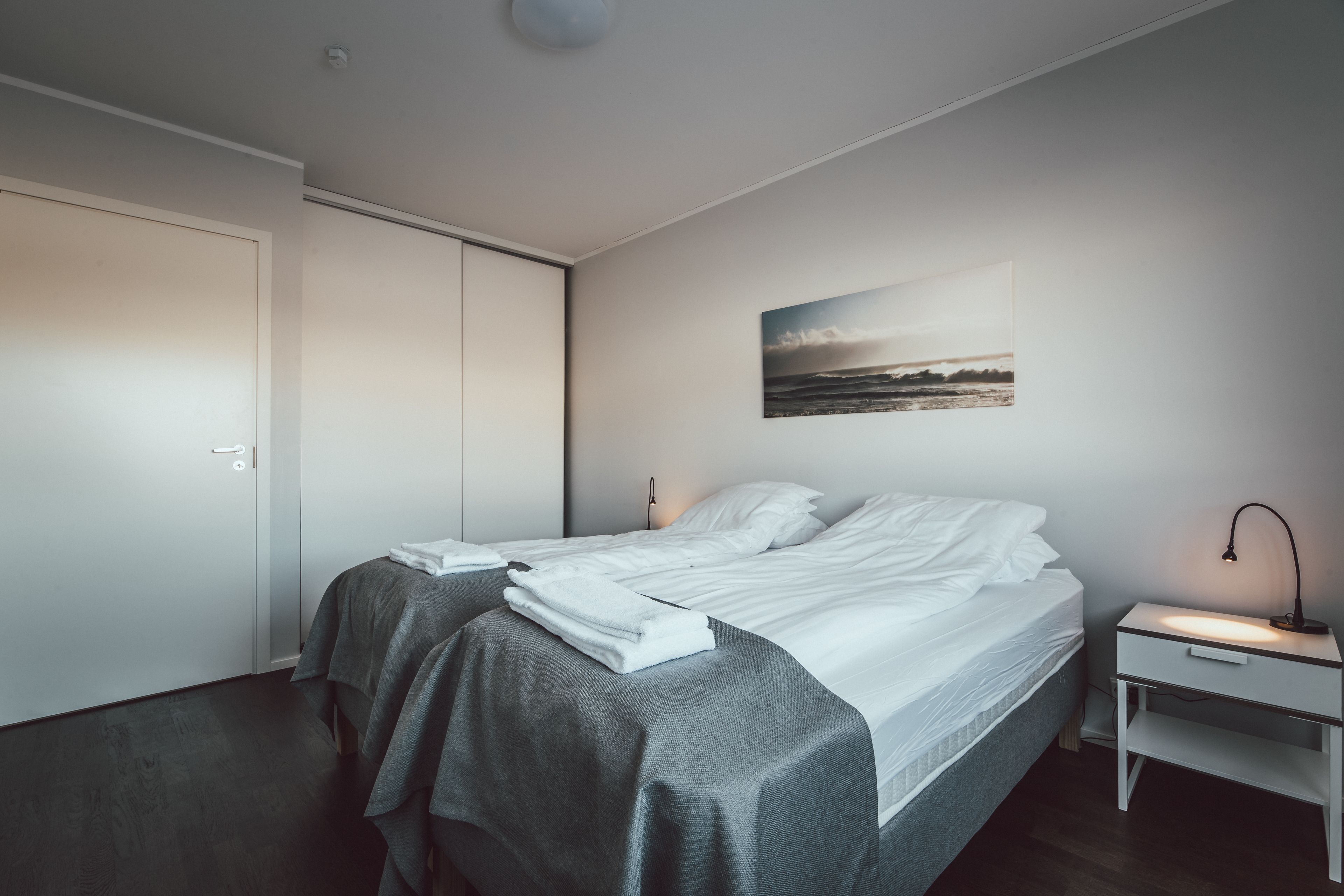 A modern bedroom with a bed, bedside tables, and a painting on the wall.