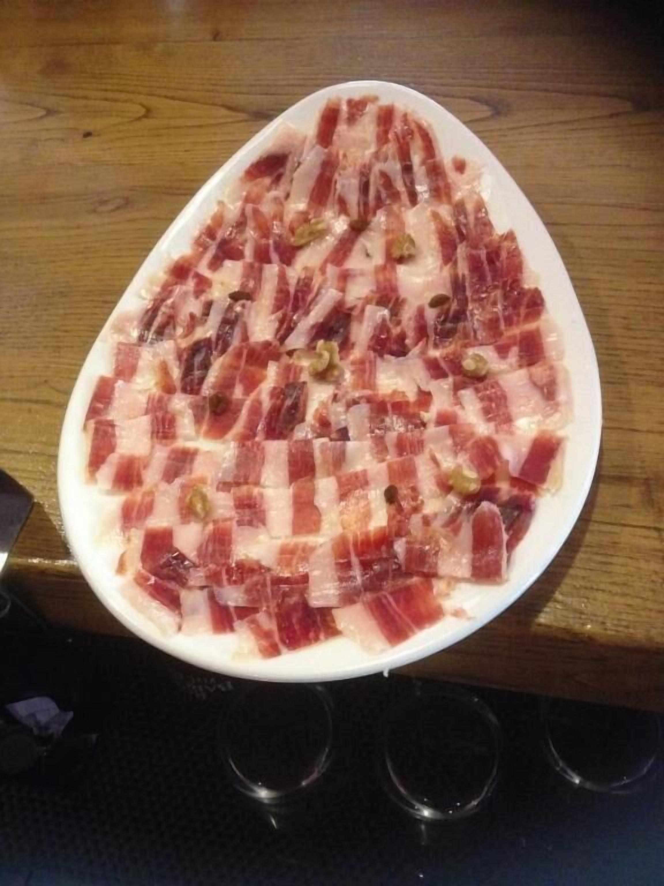A white plate with sliced cured meat on a wooden table.