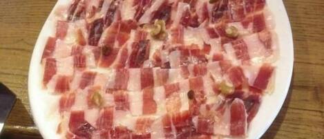 A white plate with sliced cured meat on a wooden table.