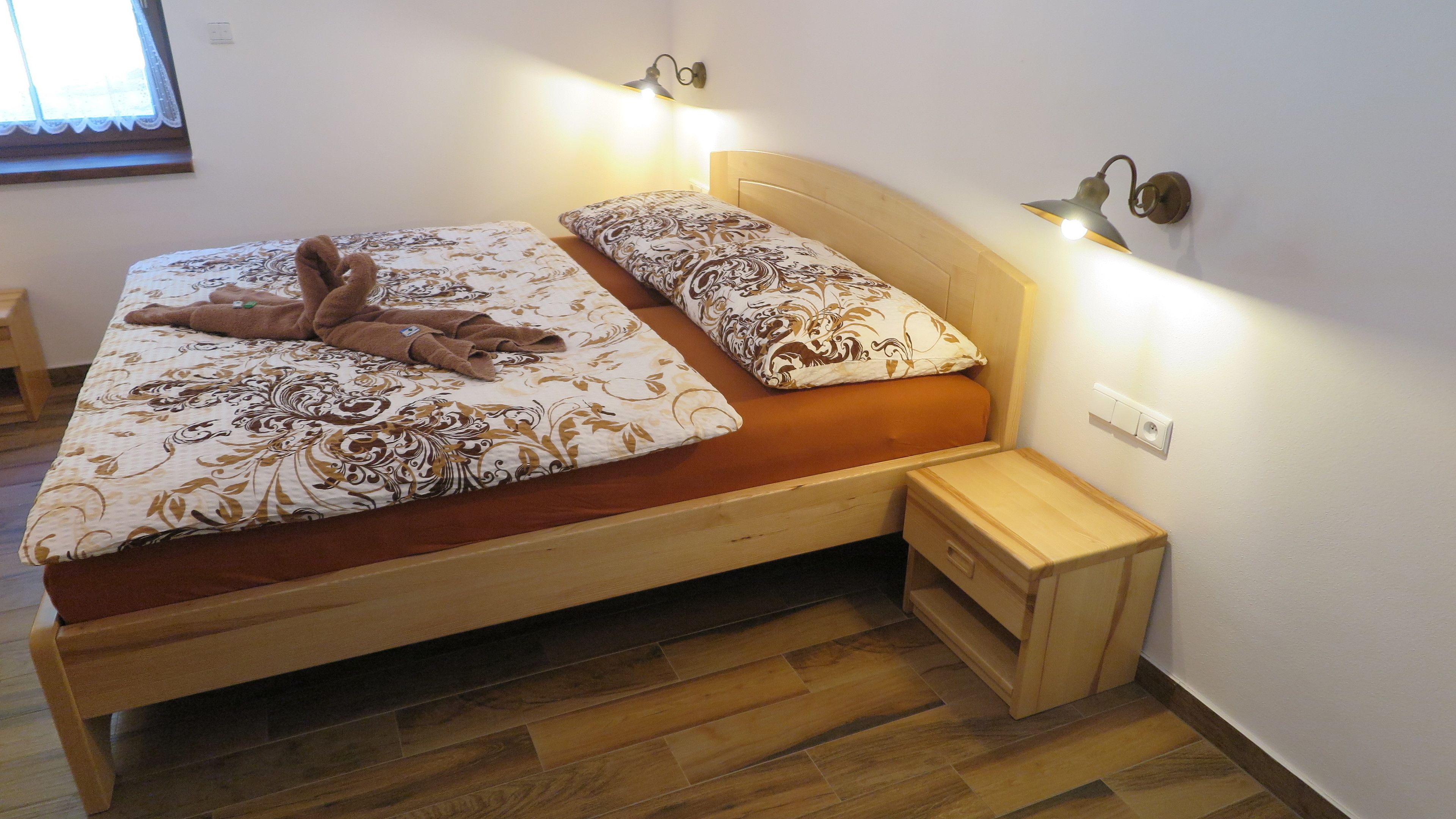 Una cama doble con cabecera y piecera de madera, una mesita de noche con cajón y dos lámparas de pared.
