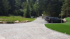 A paved pathway leading to a parking area with cars and bicycles, surrounded by greenery and trees. - Club Rezidence Pod Lučí Loučovice (Loucovice)