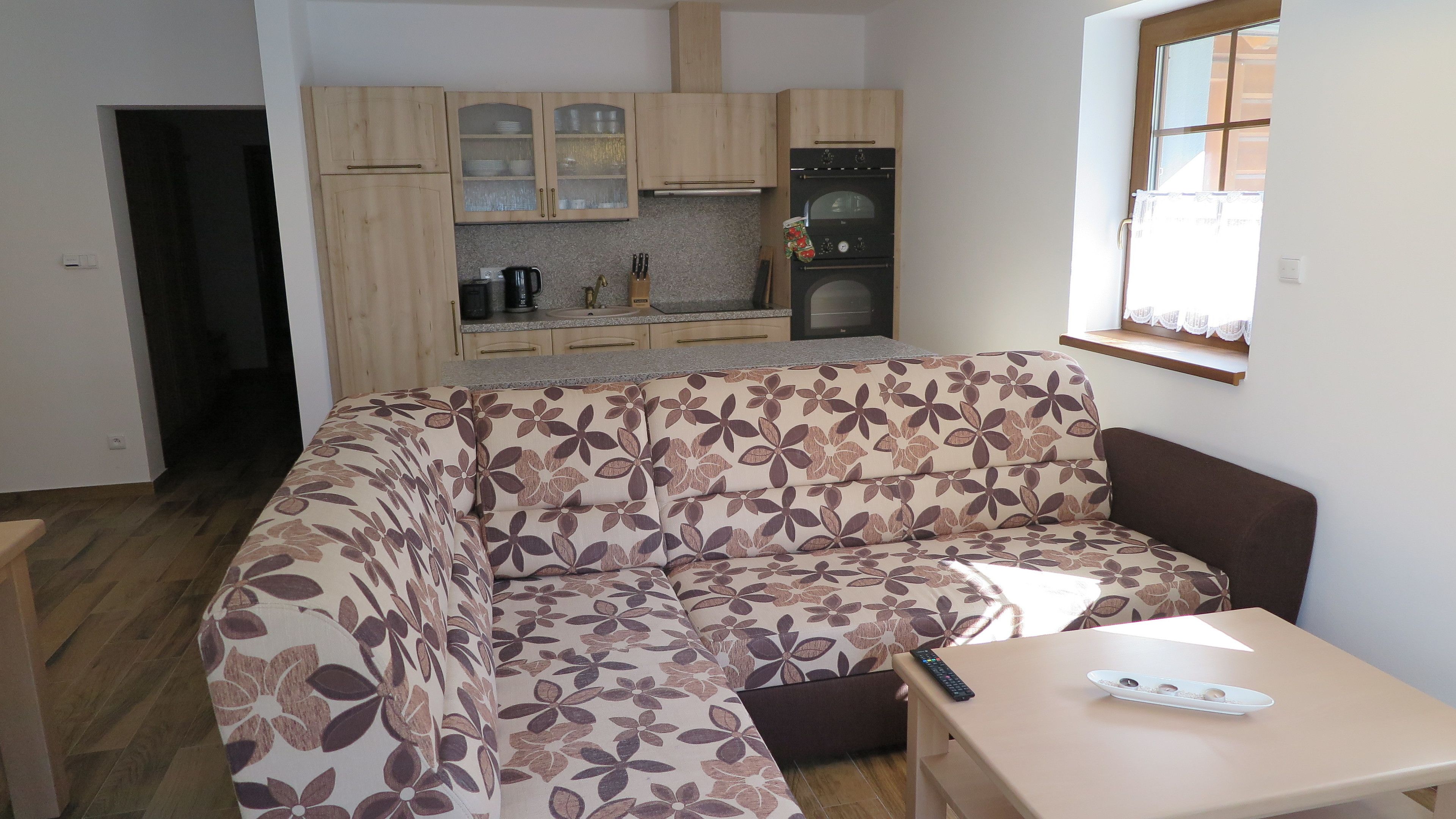 A compact living space with a sofa, a small table, a kitchen area with cabinets and appliances, and a window.
