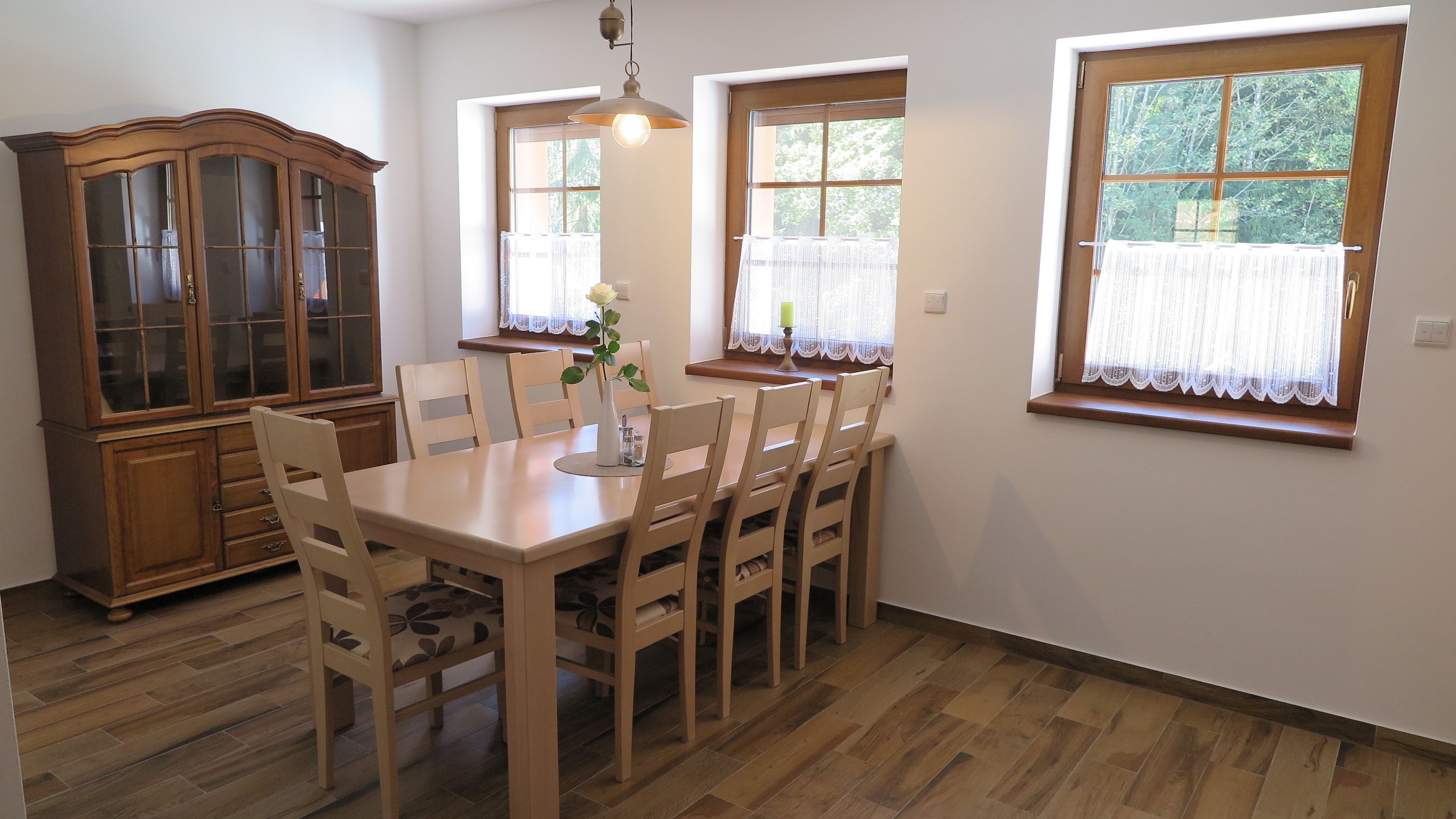 A dining area with a wooden table and chairs, a cabinet, and windows with curtains.