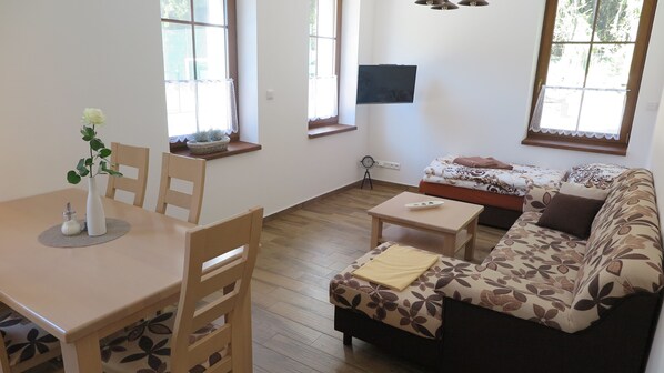 A living room with a sofa, a dining table with chairs, and a small table with a vase. - Club Rezidence Pod Lučí Loučovice (Loucovice)