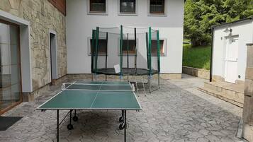 An outdoor area with a ping pong table, two trampolines, and a stone-tiled floor.
