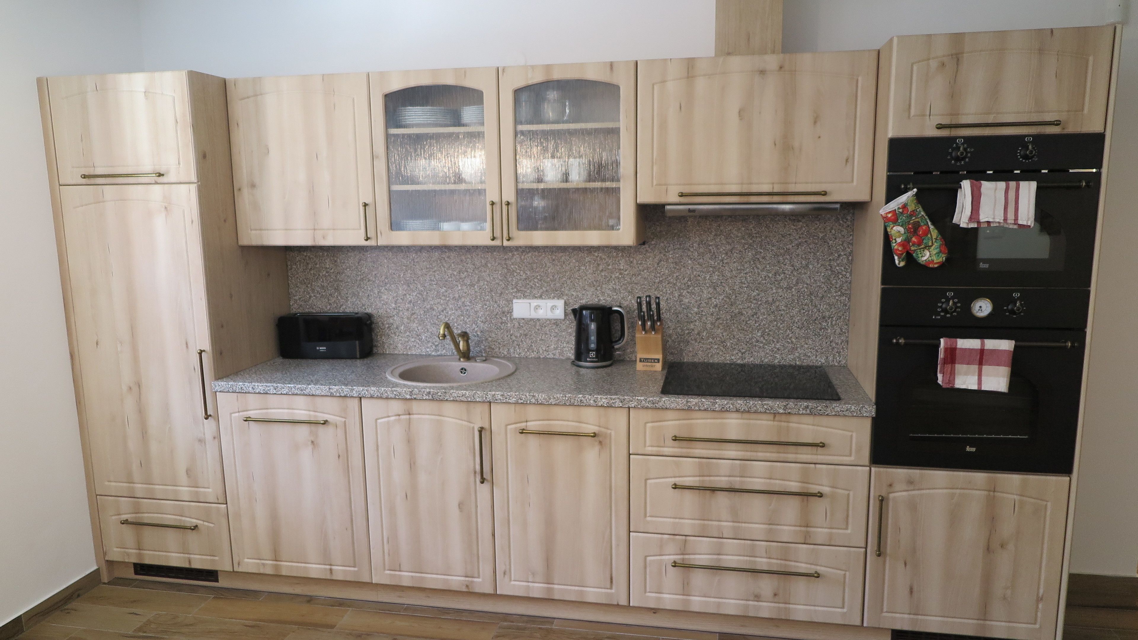 A kitchen with light wood cabinets, a granite countertop, a toaster, a kettle, and a black oven.