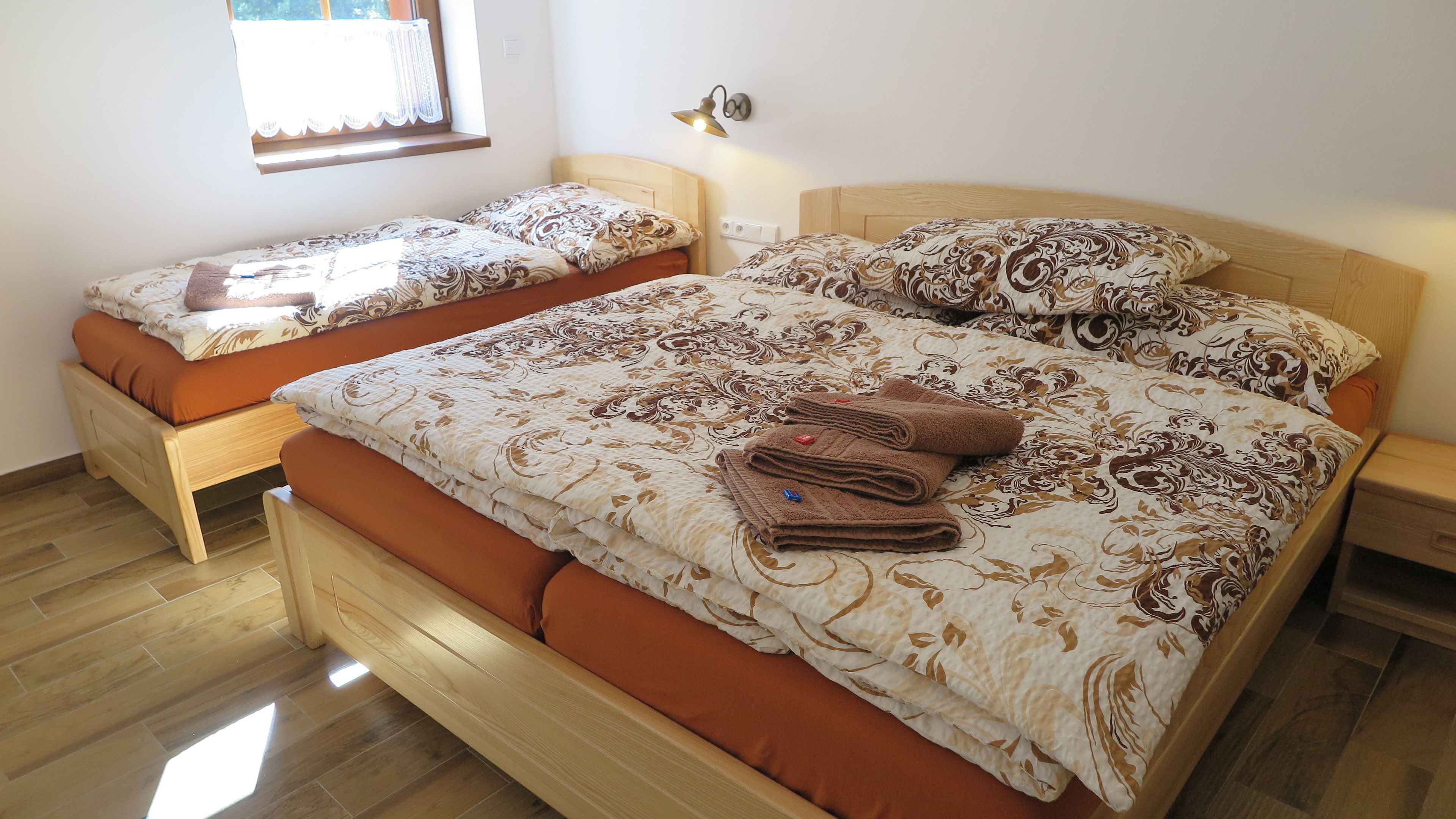 A double bed with a floral bedspread and two pillows, a smaller single bed with a similar bedspread, and a nightstand with a lamp.