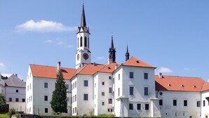 A historic building with a clock tower, reflecting in a calm body of water, surrounded by a stone wall. - Club Rezidence Pod Lučí Loučovice (Loucovice)