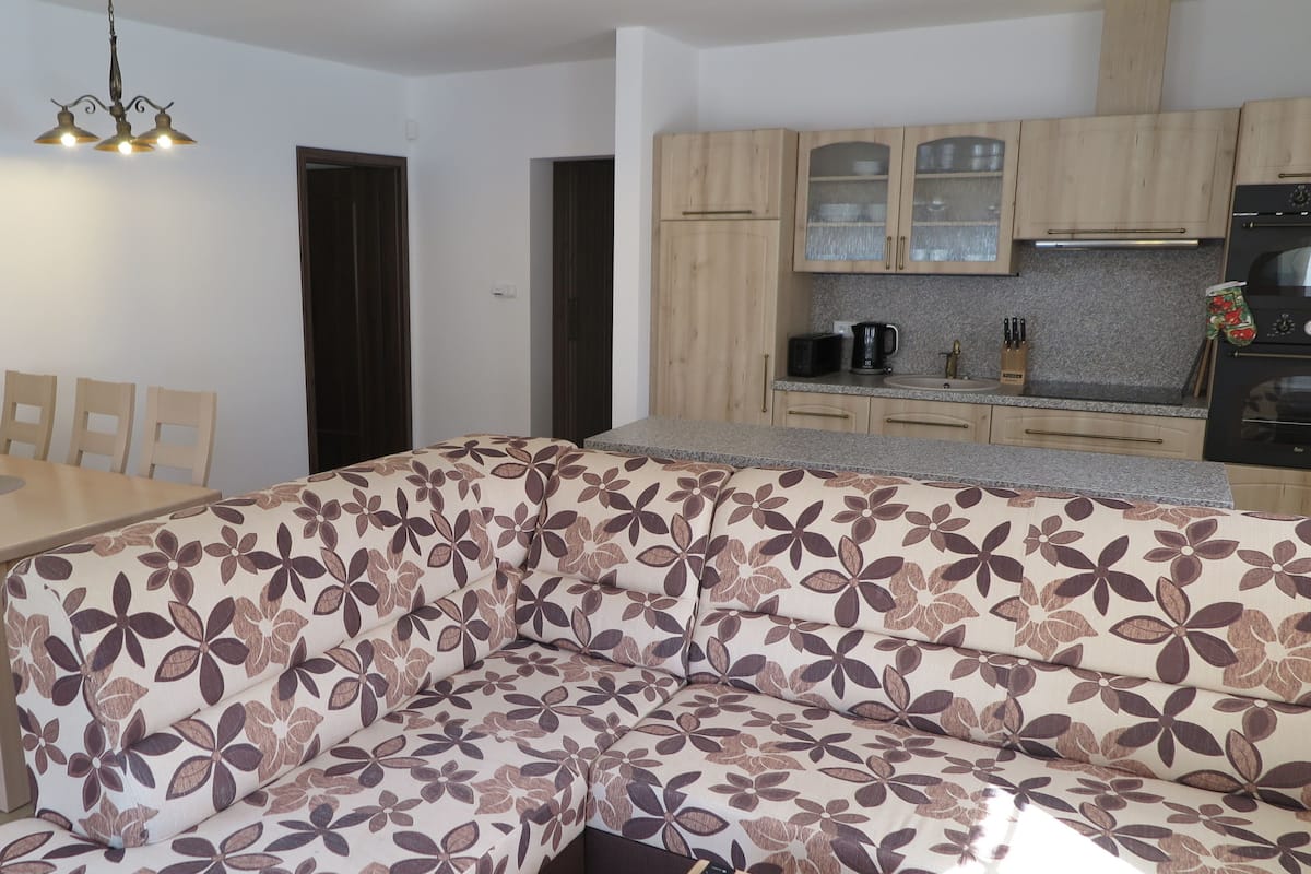 Una sala de estar moderna con un sofá floral, una mesa de comedor de madera, sillas y una cocina con armarios y electrodomésticos.
