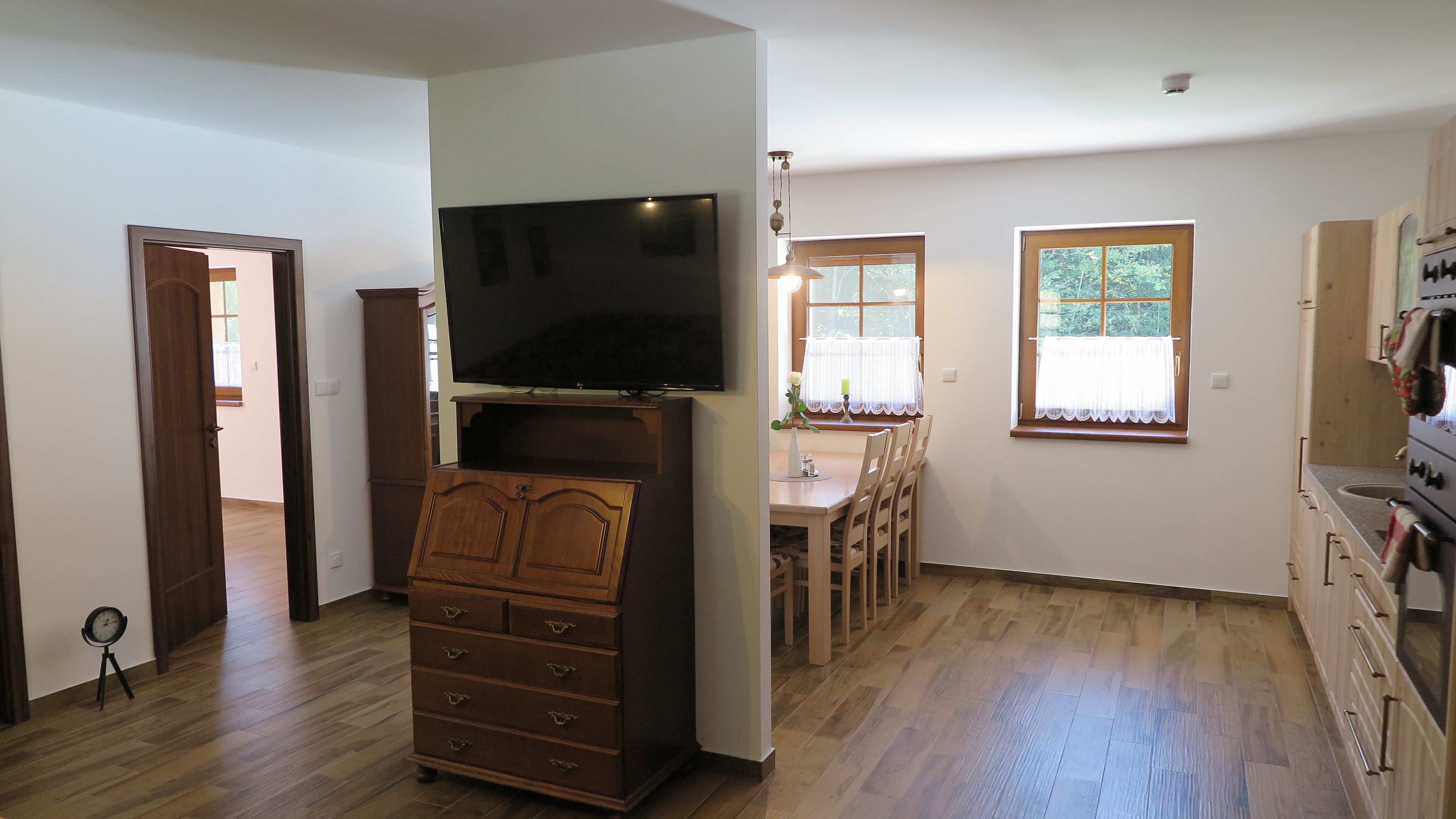 Une pièce comprenant une commode en bois, un téléviseur à écran plat, une table à manger avec des chaises et un coin cuisine équipé d’une cuisinière.