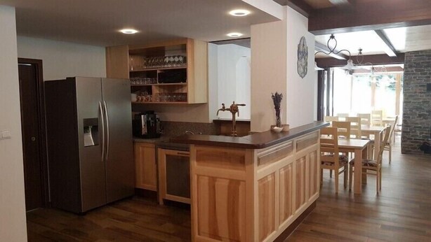 A kitchen with wooden cabinets, a refrigerator, and a dining area with a table and chairs. - Club Rezidence Pod Lučí Loučovice (Loucovice)