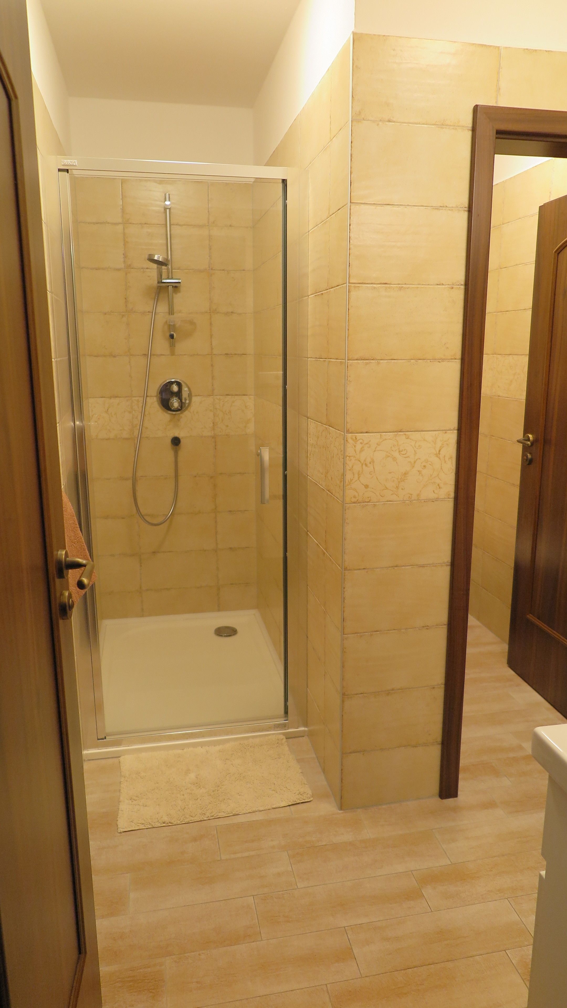 A walk-in shower with a glass door, beige tiled walls, and a wooden floor.