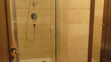 A walk-in shower with a glass door, beige tiled walls, and a wooden floor.
