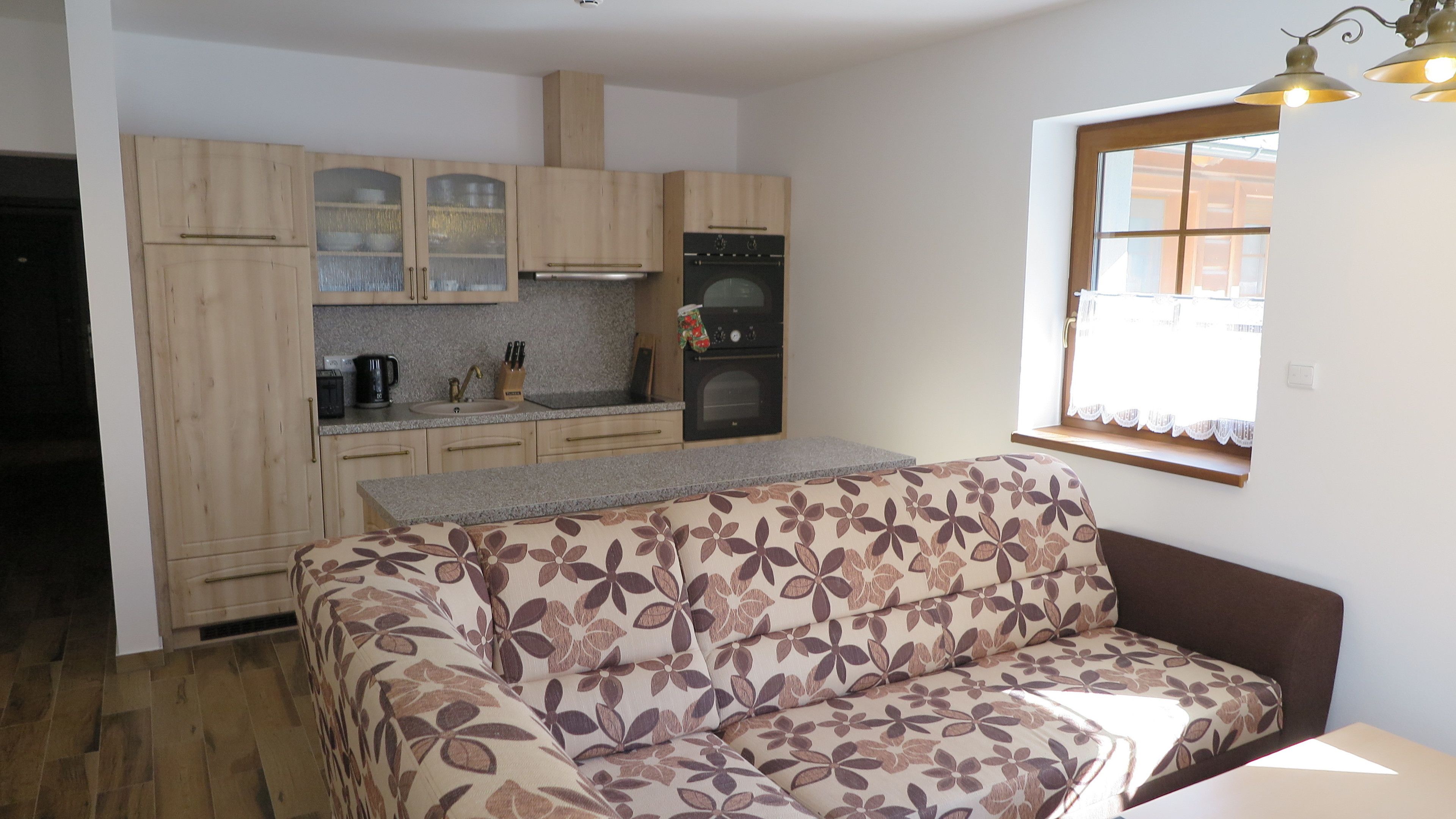 A compact kitchen with wooden cabinets, a built-in oven, and a window with lace curtains.