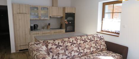 A compact kitchen with wooden cabinets, a built-in oven, and a window with lace curtains.