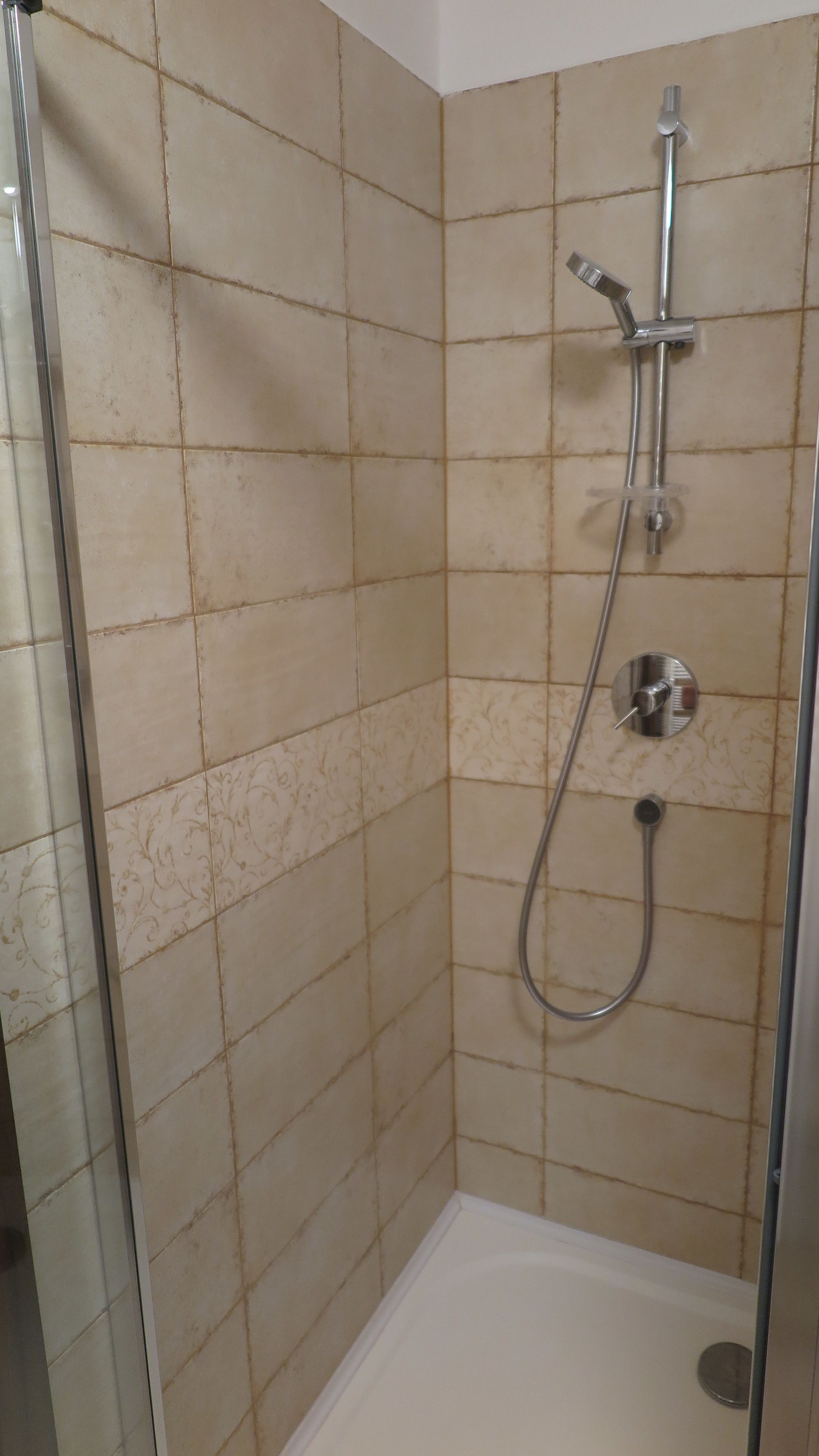 Un área de ducha con azulejos color beige, una puerta de cristal y un cabezal de ducha manual.