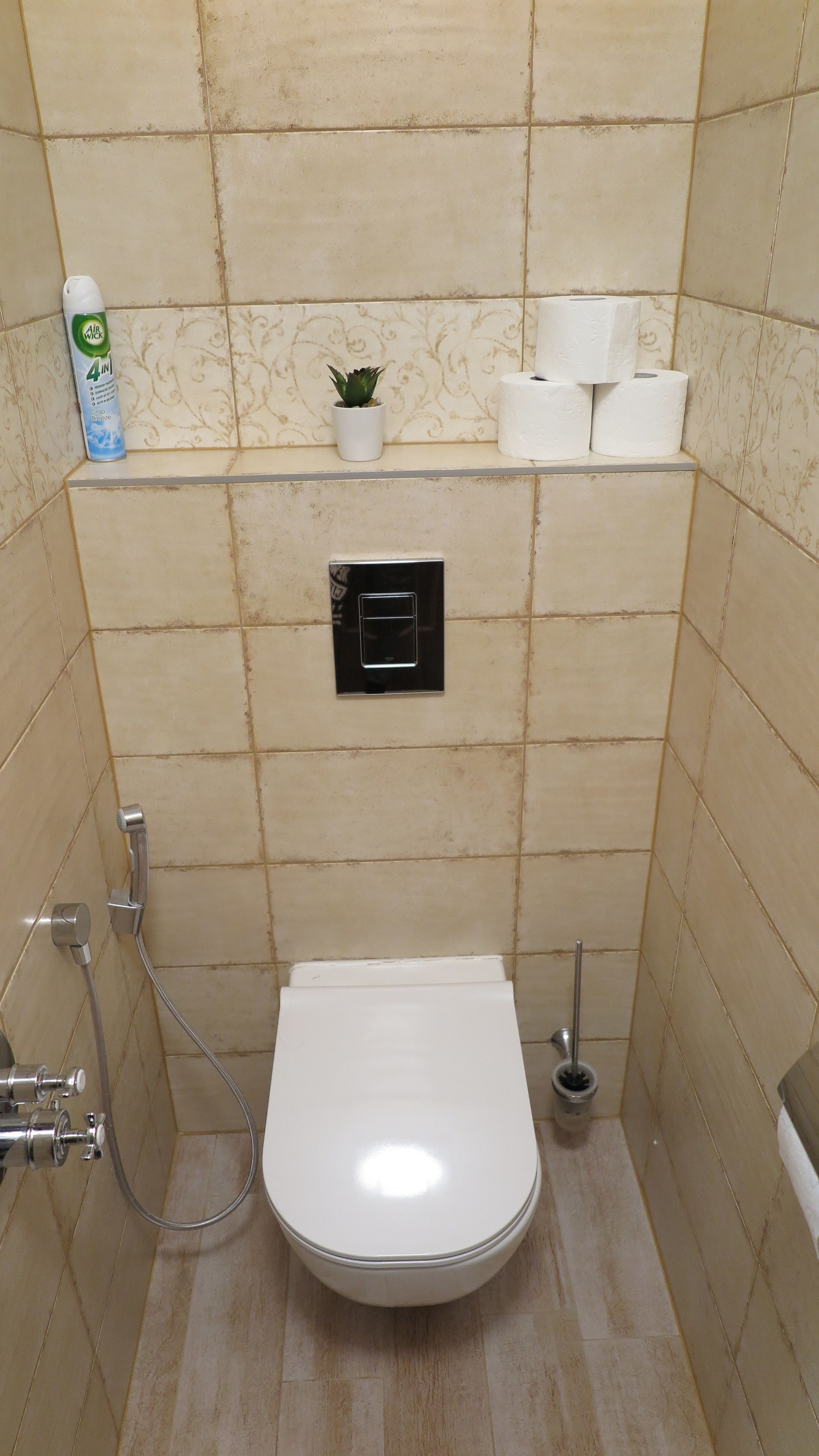 Un bagno piccolo rivestito di piastrelle, con il water, una doccia e uno scaffale con una pianta e carta igienica.