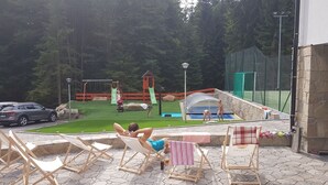 An outdoor swimming pool area with a slide, a small play structure, and lounge chairs. - Club Rezidence Pod Lučí Loučovice (Loucovice)