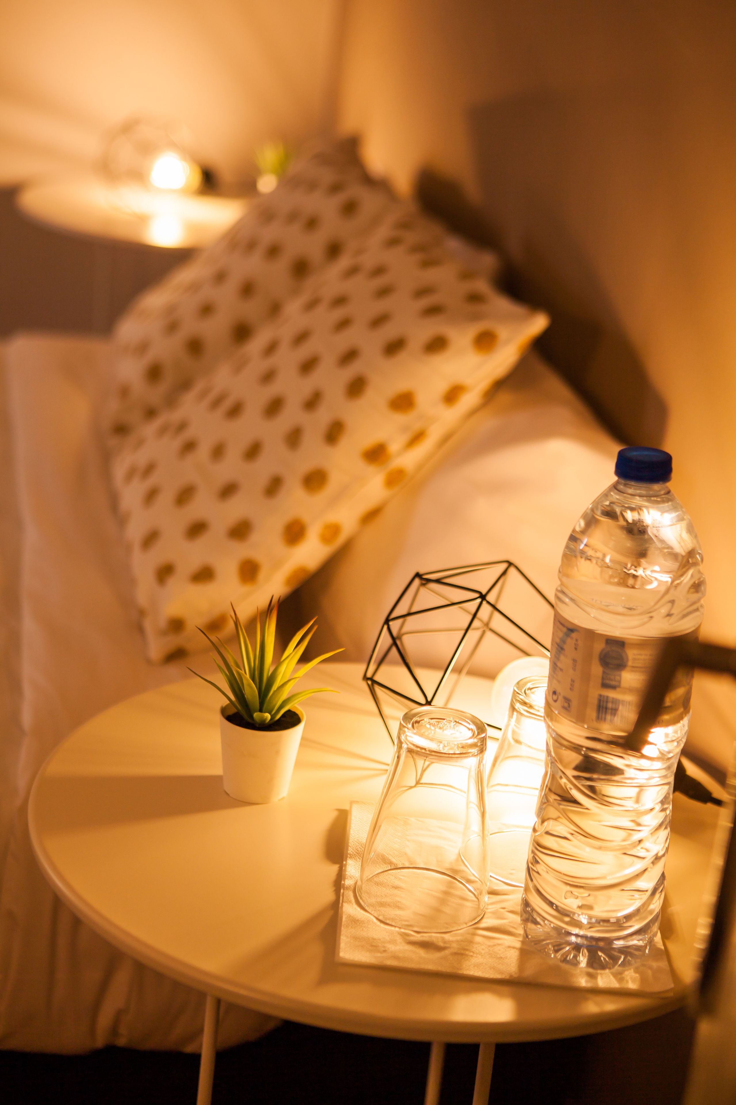 A small round table with a water bottle, a glass, and a potted plant.
