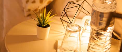 Une petite table ronde avec une bouteille d’eau, un verre et une plante en pot.