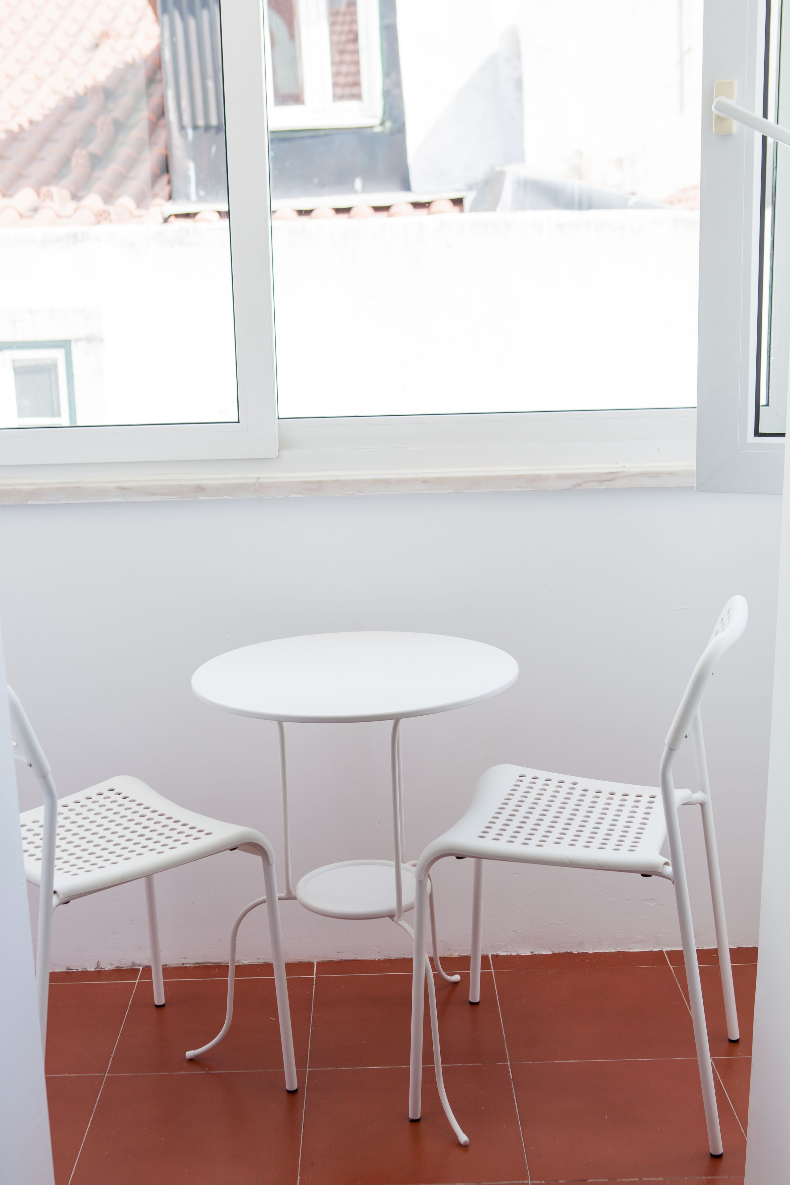 Ein kleiner, weißer Tisch mit zwei weißen Stühlen in einem Raum mit Fliesenboden und Fenster.