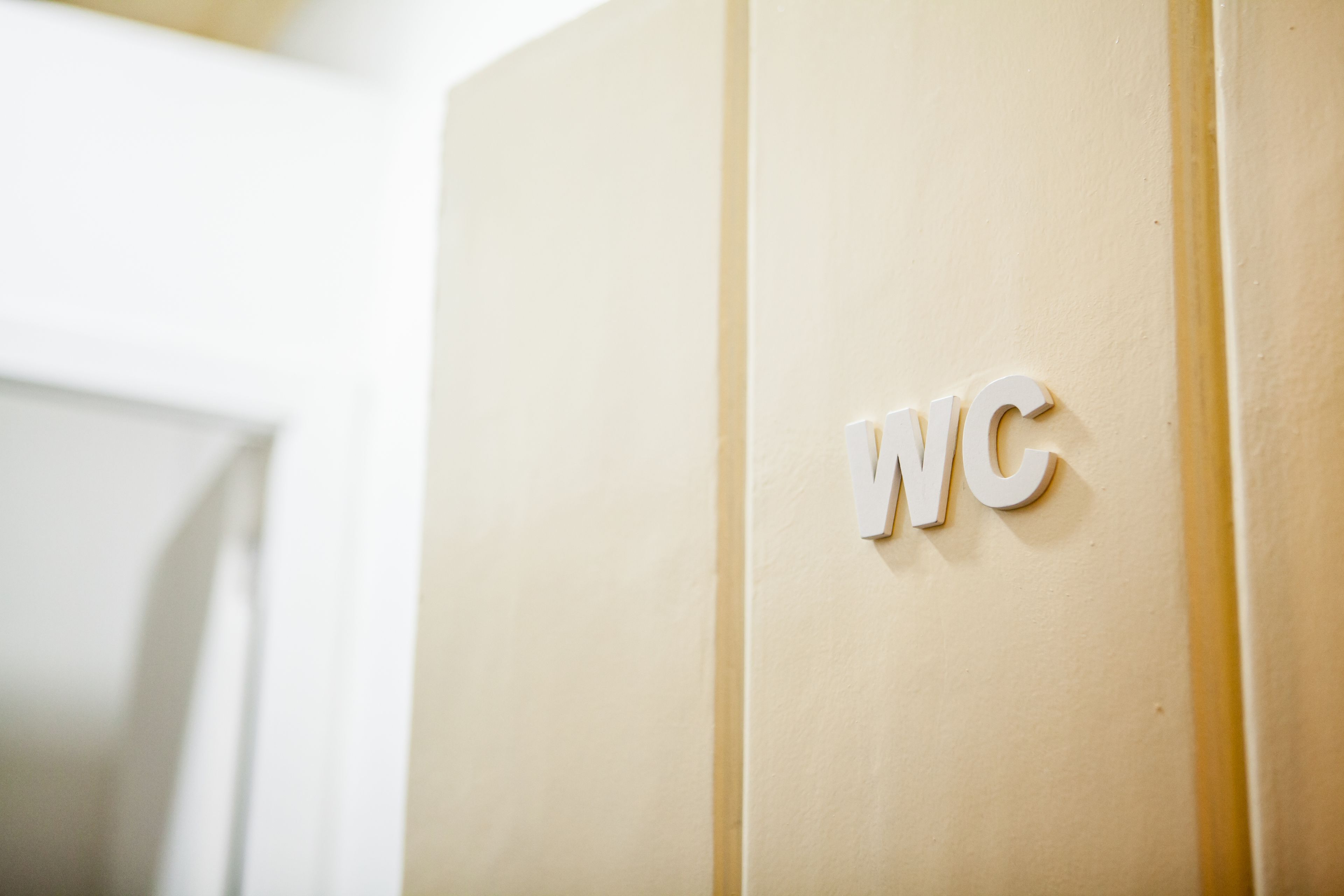 Un letrero de baño con las letras 'WC' sobre una pared color beige.