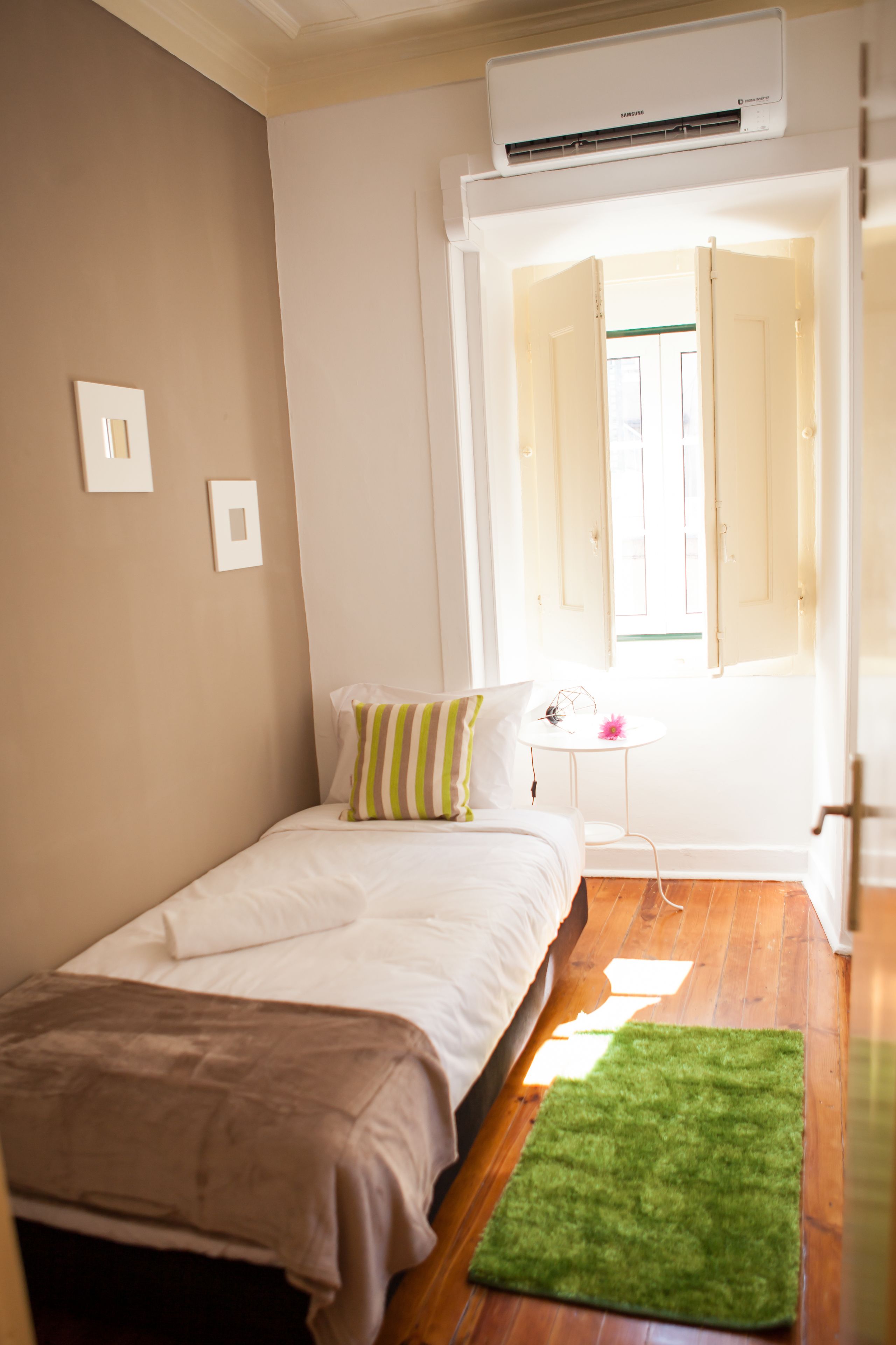 Une chambre à coucher avec un lit, une petite table, un tapis vert et un appareil de climatisation.