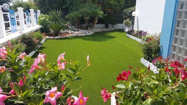 A well-maintained garden with a green lawn, various flowering plants, and a white fence with decorative elements. - Hotel Le Palme (Sabaudia)